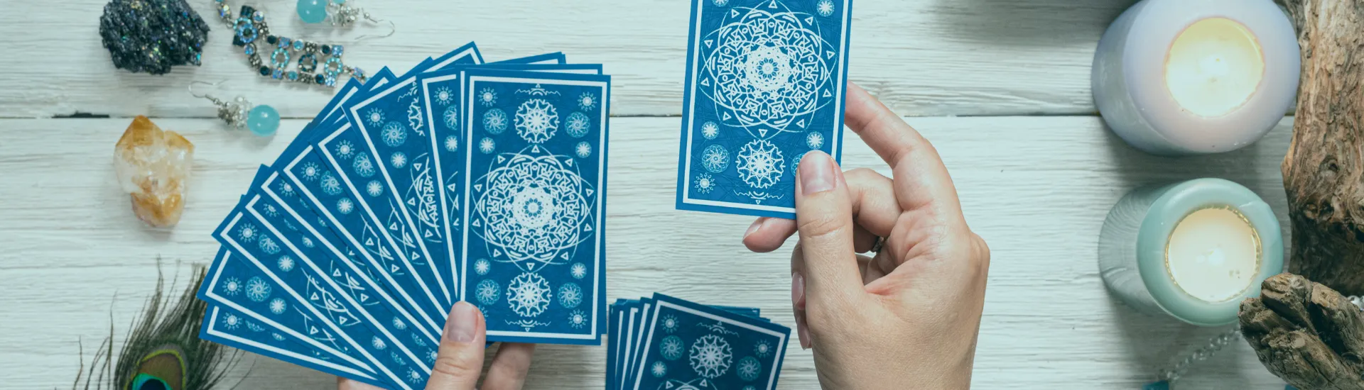 Hands laying out a spread of tarot cards beside candles and crystals